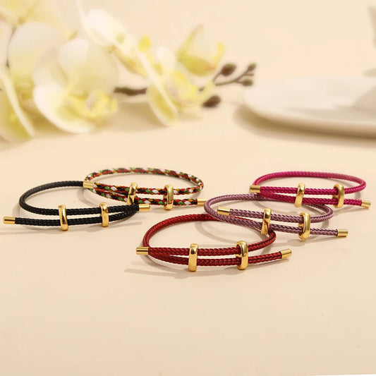 Set of four braided bracelets with gold accents on a beige surface with blurred flowers in the background