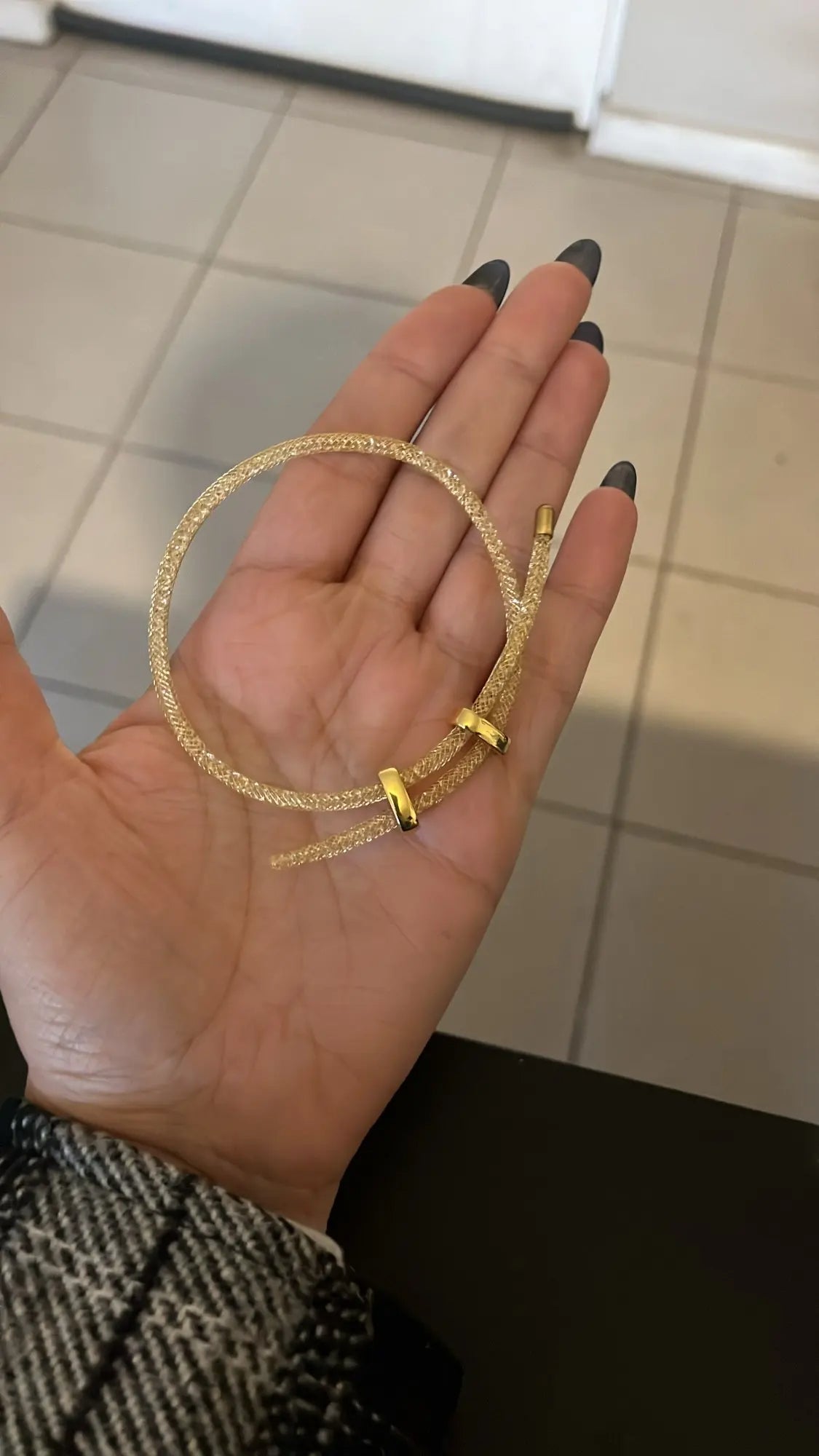 Gold bracelet held in a hand against a tiled floor background