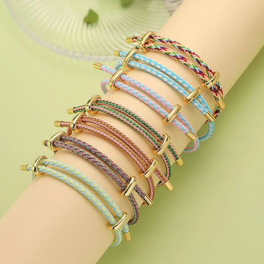 Multicolored braided bracelets with gold accents on a wrist against a light green background