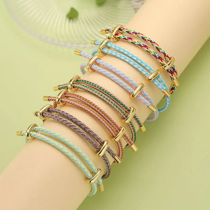 Multicolored braided bracelets with gold accents on a wrist against a light green background